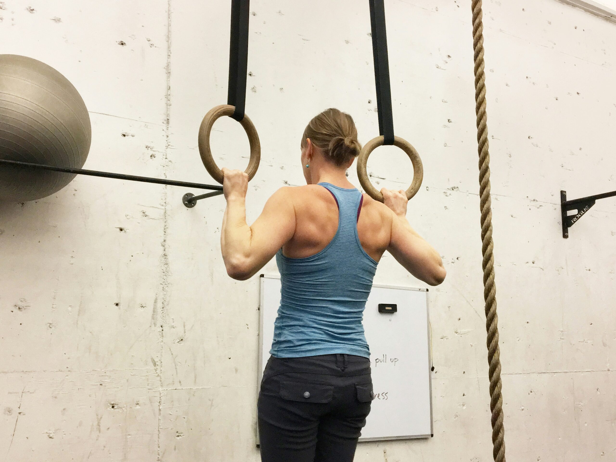 Exercício de Calistenia para as costas: Mulher fazendo barra fixa na argola com uma camiseta regata azul e uma calça legging preta.