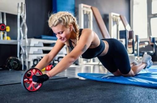 Mulher loira fazendo exercicio com Roda Abdominal na academia.